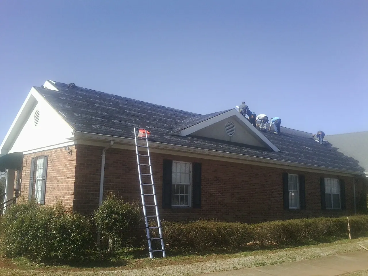 Crew tearing shingles off a brick ranch roof with a ladder set — Metal Roof Repair work by our crew in Snowville