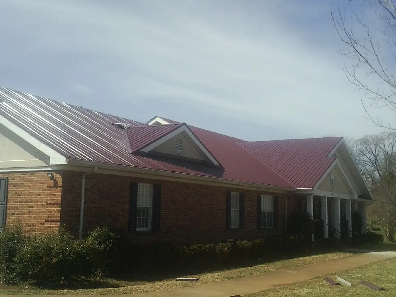 Red metal roof with gabled entries on a long brick building, from a Hail Damage Roof Repair job in Snowville