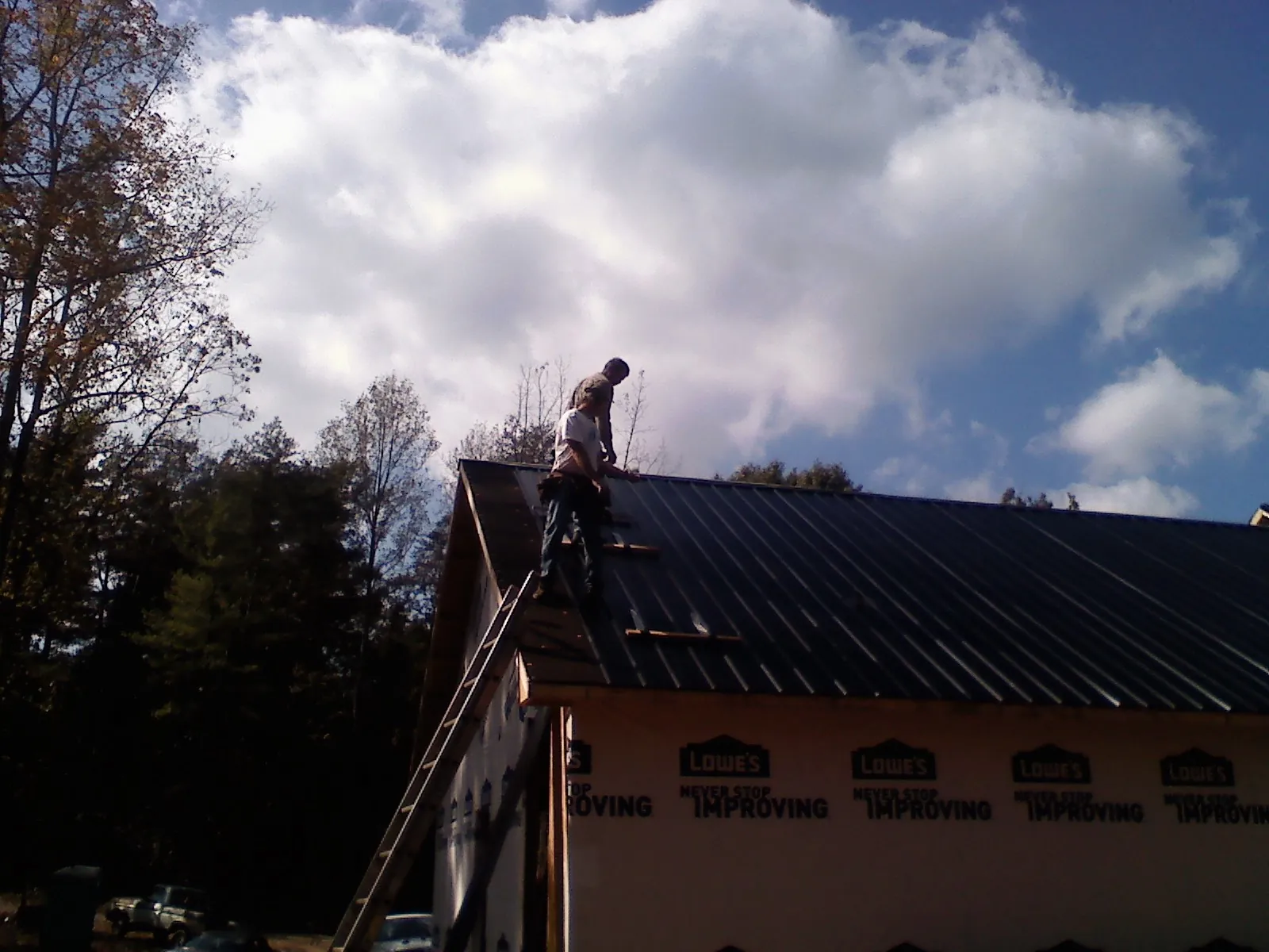 Roofer fastening dark metal panels high against a cloudy sky, from a Roof Inspection job in Snowville