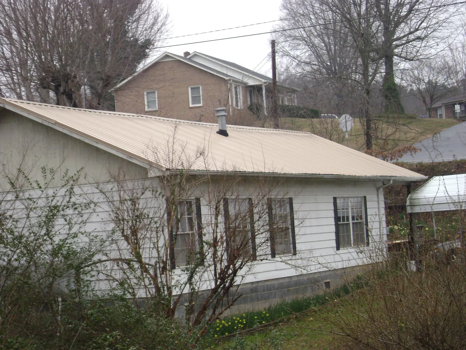 Tan metal roof on a white sided house set into a hillside — Commercial Roofing by Roofing Brothers in Snowville